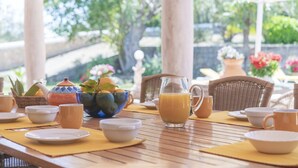 Une table dressée avec des aliments pour le petit-déjeuner, notamment une carafe de jus d’orange, des bols et un panier de fruits.