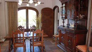 Un coin repas avec une table et des chaises en bois, un buffet orné de sculptures et une grande porte en arc de cercle.