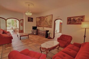 Un salon avec des canapés rouges, une table basse en bois, un lustre et un grand tableau accroché au mur.