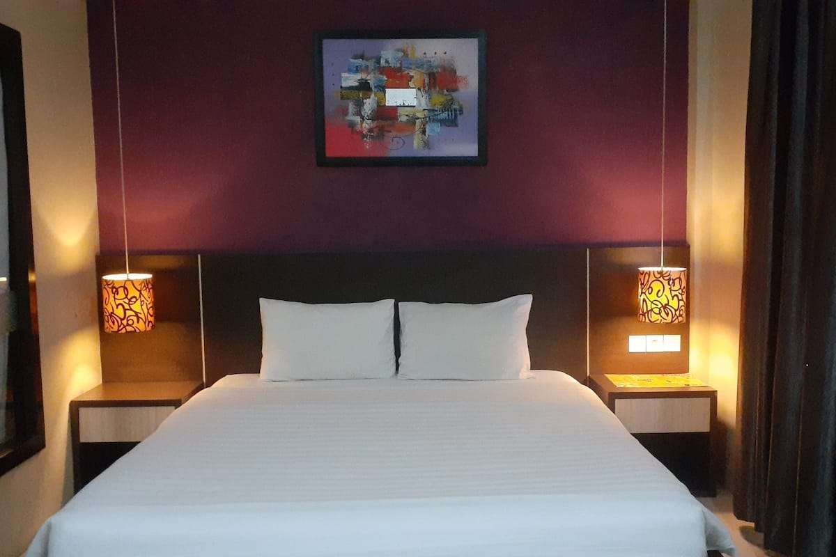 A hotel room with a large bed, two bedside lamps, and a framed abstract painting on the wall.