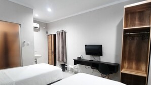 A hotel room with two beds, a desk with a TV, a wooden wardrobe, and a bathroom with a mirror and sink. - Rahat Icon Hotel (Tanjung Pandan)