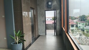 A hallway with a potted plant, a clock, and a view of buildings outside. - Rahat Icon Hotel (Tanjung Pandan)