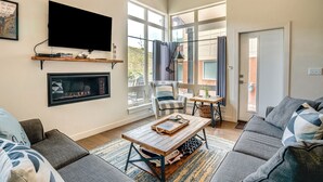 Ein Wohnzimmer mit Kamin, Flachbildfernseher, Sofa, Couchtisch und Blick ins Freie durch große Fenster.