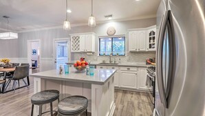 A modern kitchen with white cabinetry, a stainless steel refrigerator, and a central island with stools. - Pet-Friendly Flagstaff Escape w/ Fenced-In Yard! (Flagstaff)