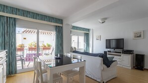 Un salon avec un téléviseur, un canapé, une table à manger avec des chaises et un balcon avec vue.