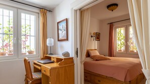 Ein Schlafzimmer mit einem Bett, einem Schreibtisch mit Laptop, einem Stuhl und einem Fenster mit Vorhängen.