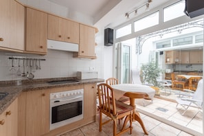 A kitchen with wooden cabinets, a built-in oven, and a dining area with a table and chairs. - Cozy Apartment with Sunny Patio, Barbecue, Wi-Fi & Air Conditioning (Nerja)