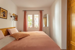 A bedroom with a bed, a window with curtains, a bedside table, a mirror, and a wardrobe. - Cozy Apartment with Sunny Patio, Barbecue, Wi-Fi & Air Conditioning (Nerja)