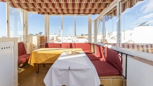 Eine sonnendurchflutete Terrasse mit Tisch, roten Sitzgelegenheiten und großen Fenstern mit Blick auf die Stadt.