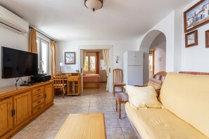 A living room with a TV, wooden furniture, a sofa, and a dining area. - Cozy Apartment with Sunny Patio, Barbecue, Wi-Fi & Air Conditioning (Nerja)