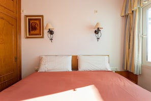 A bedroom with a bed, two wall-mounted lamps, a framed picture, and a window with curtains. - Cozy Apartment with Private Terrace, Roof Top and Air Conditioning (Nerja)