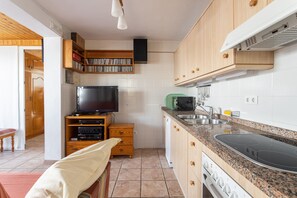 A compact kitchen with wooden cabinets, a built-in TV, a microwave, and a dishwasher. - Cozy Apartment with Private Terrace, Roof Top and Air Conditioning (Nerja)