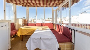 A sunlit patio with a table and red seating, large windows, and a view of buildings. - Cozy Apartment with Private Terrace, Roof Top and Air Conditioning (Nerja)