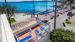 Een balkon met blauwe kussens, een geplaveid pad, palmbomen en uitzicht op zee.