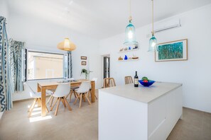 A modern kitchen with a central island, pendant lights, and a view through the window.