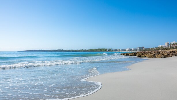 Een strand met helderblauw water, een zandstrand en een stadsachtergrond.
