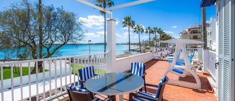 A balcony with a glass table and chairs, overlooking a beach and palm trees.