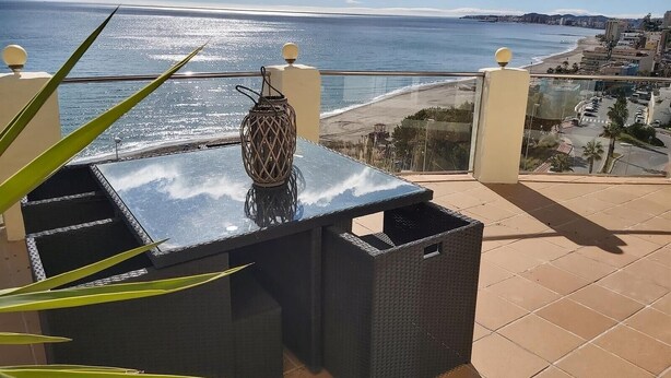 Ein Balkon mit Tisch, einer Korlampen und Blick auf das Meer und die Stadt.