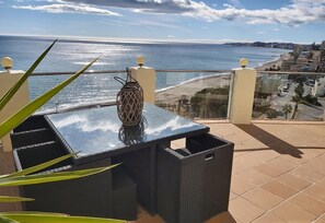 Ein Balkon mit Tisch, einer Korlampen und Blick auf das Meer und die Stadt.