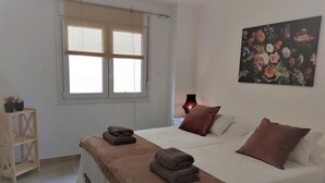 Ein Schlafzimmer mit einem Bett, Kissen, einer Nachttischlampe, einem Fenster und einem Bild an der Wand.