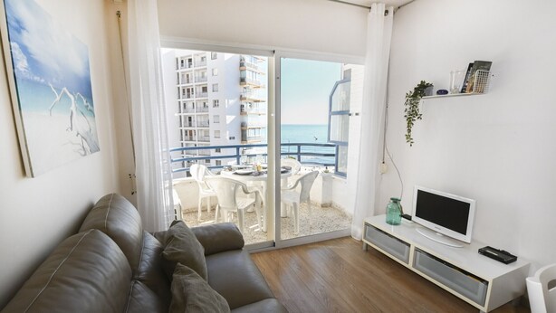 Un soggiorno moderno con un divano, TV e un balcone vista mare e edifici.