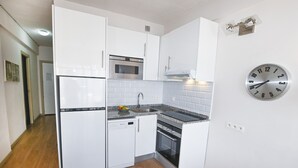 Una cucina compatta con mobili bianchi, un forno a microonde integrato, una lavastoviglie e un piano cottura.