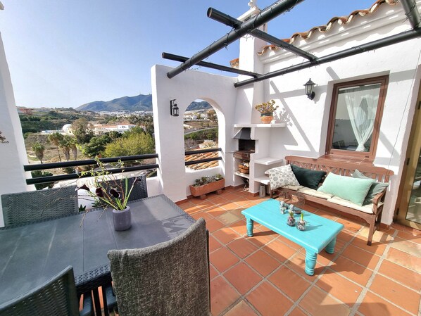 A balcony with a table, chairs, a sofa, and a view of the cityscape.