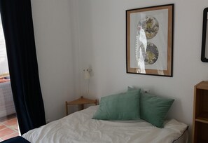 A bedroom with a bed, two pillows, a nightstand, a lamp, and a framed picture on the wall.