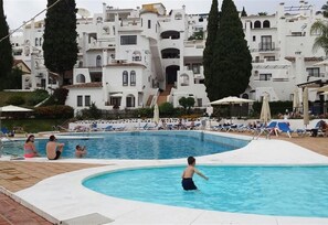 A swimming pool with lounge chairs and a building with white architecture in the background.
