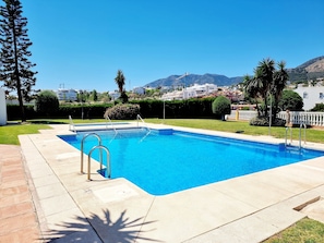 A rectangular swimming pool with a clear blue water, surrounded by a tiled deck, with a view of buildings and mountains in the background. - Great Townhouse 400m from the Beach with Sea View, Wi-Fi and Air Conditioning (Benalmádena)