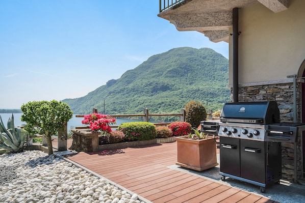 A patio with a grill, potted plants, and a view of a lake and mountains.