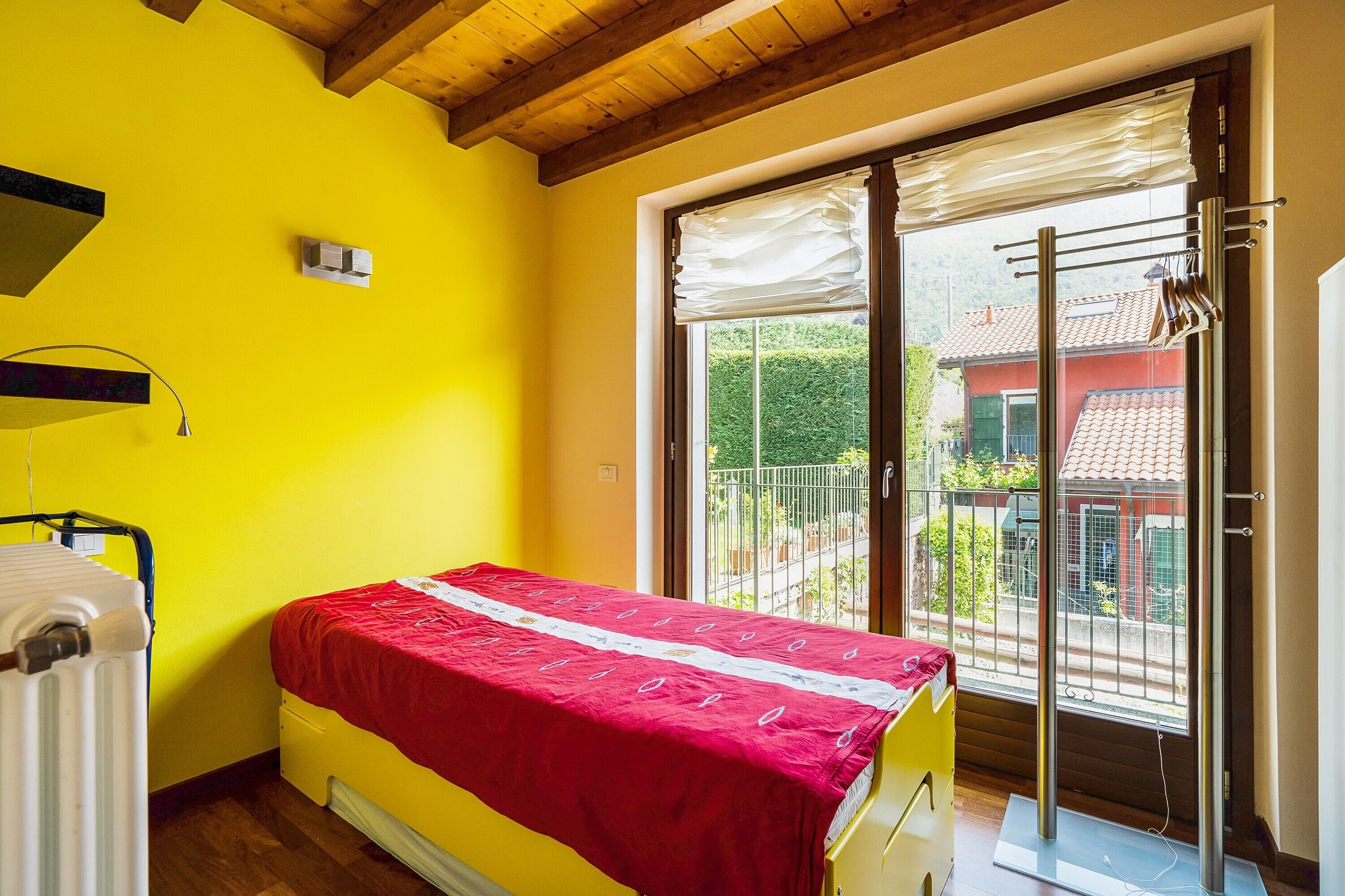 A room with a bed, a radiator, a window with a view, and a balcony.