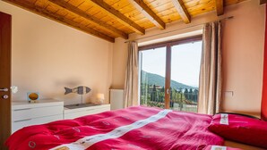 Un dormitorio con una cama grande, techo de madera, ventana con cortinas y vistas a montañas.