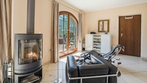 Una sala de estar con chimenea, sofá, mesa de comedor y vistas a través de un ventanal grande.