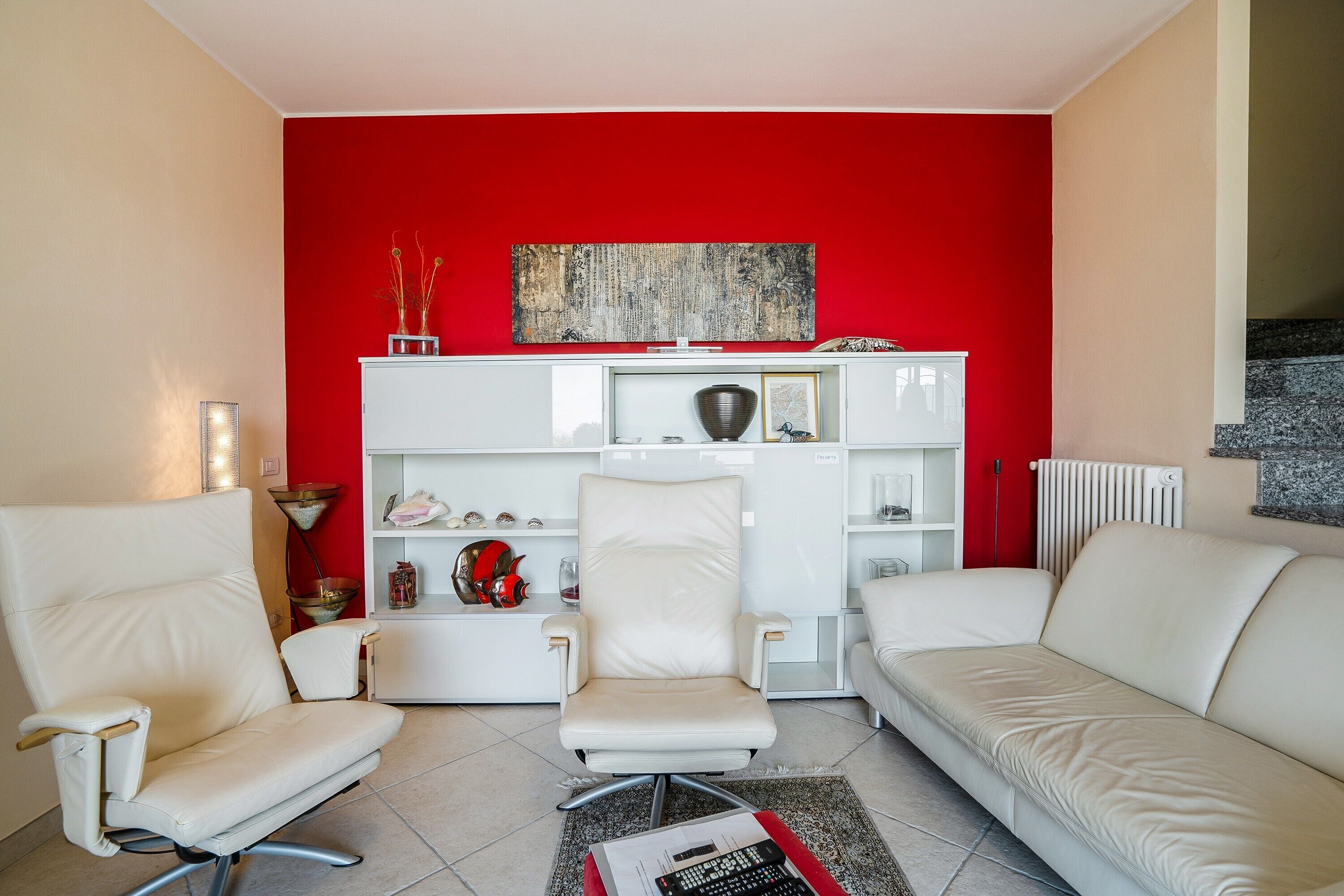 Un soggiorno con una parete decorata in rosso, arredi bianchi e un arredamento dallo stile moderno.