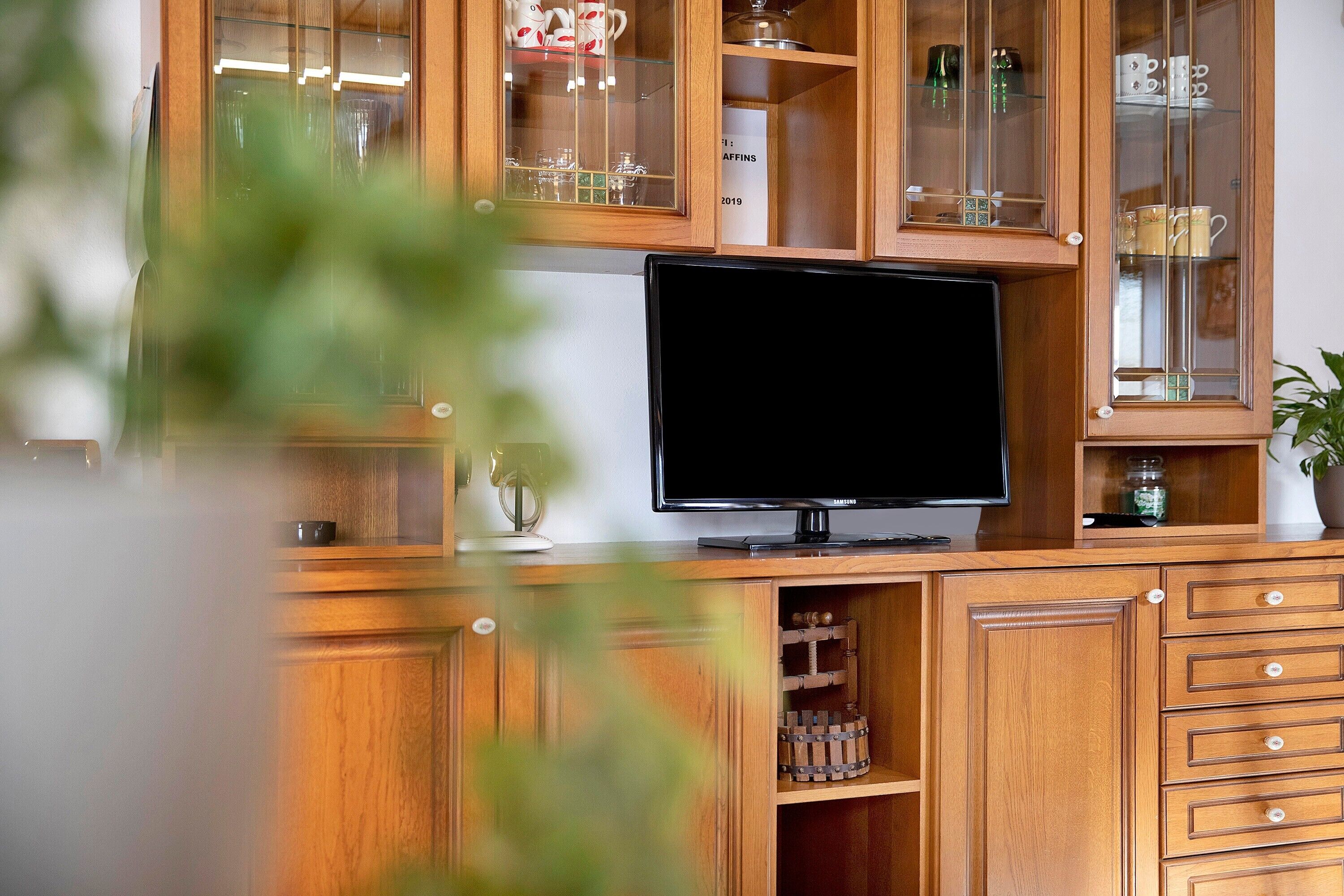 Un mueble de madera con puertas de cristal, un televisor de pantalla plana y distintos utensilios de cocina.