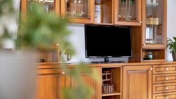 Un mueble de madera con puertas de cristal, un televisor de pantalla plana y distintos utensilios de cocina.