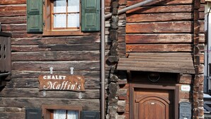 Tunnelmallinen hirsihökkelö, jonka edessä on kyltti, jossa lukee ”Chalet Maffin’s”, ja jossa on puuovi sekä postilaatikko.