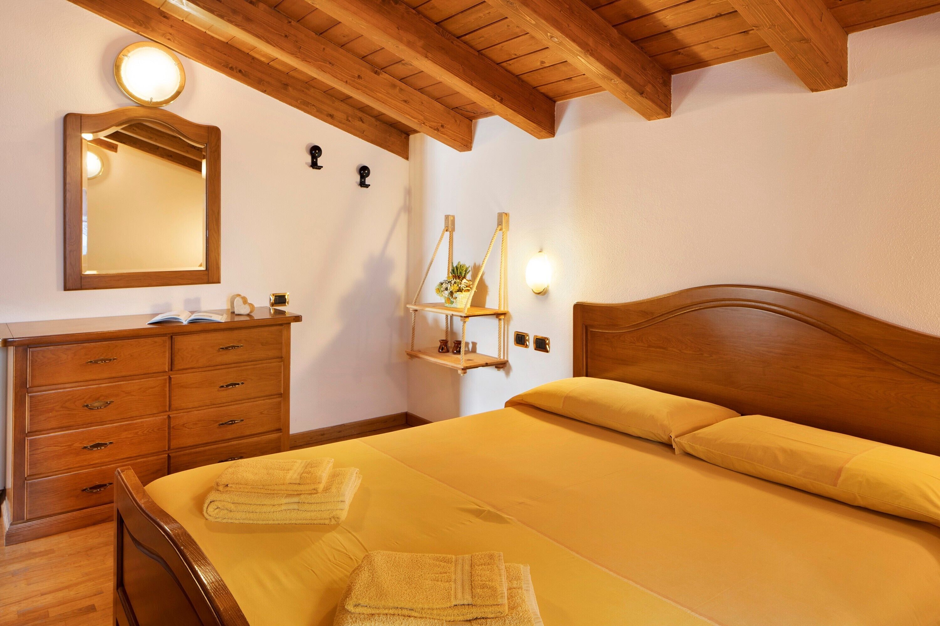 A bedroom with a wooden headboard, a bedside table, a mirror, and a wall-mounted shelf with a plant.