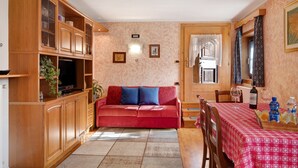 Ein Wohnzimmer mit einem roten Sofa, Holzschränken, einem Fernseher und einem Essbereich mit Tisch für zwei Personen.