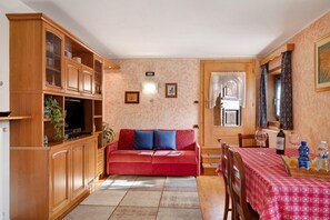 A living room with a red sofa, wooden cabinets, a television, and a dining area with a table set for two.