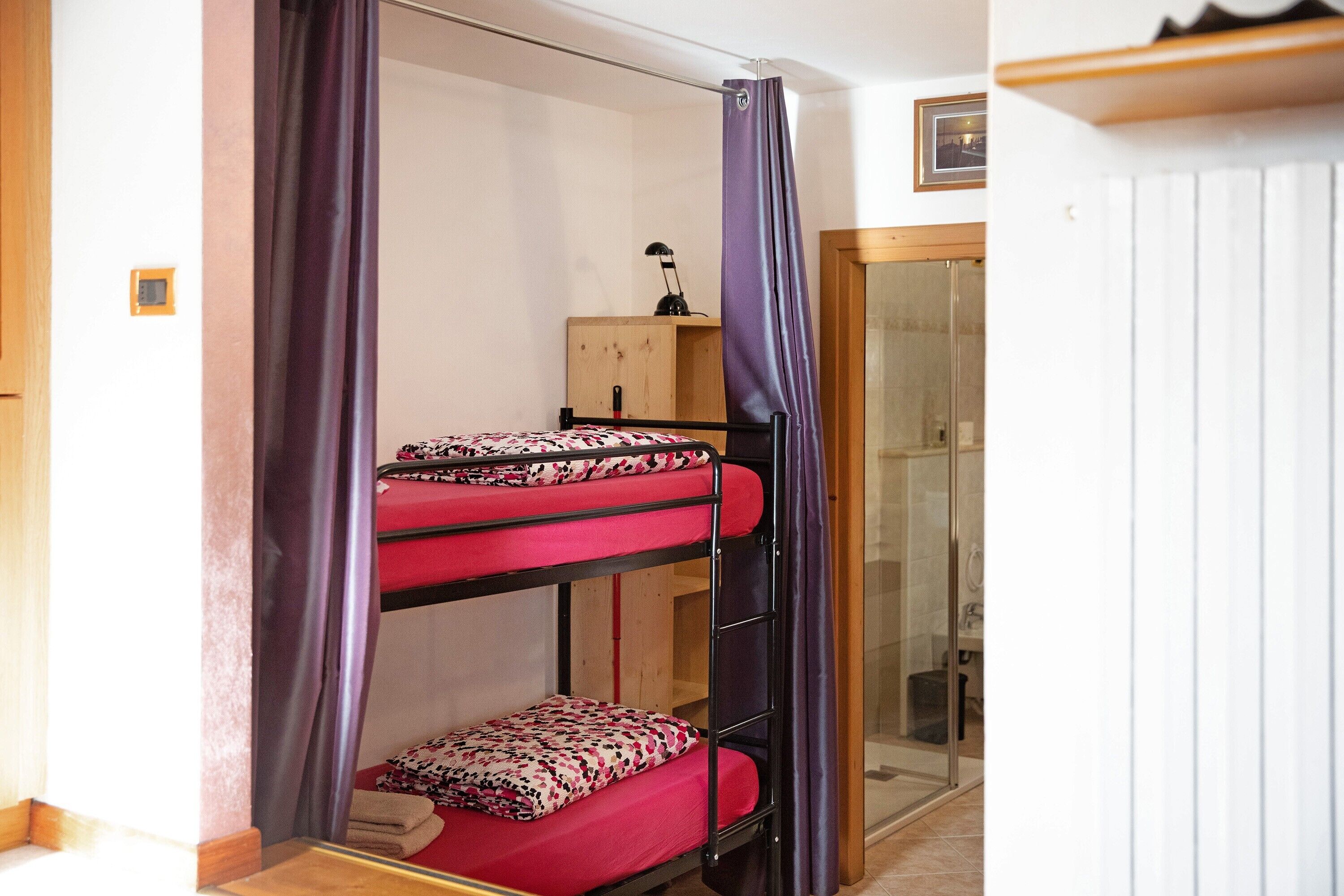 A bunk bed with a desk and chair, a shower, and a wooden cabinet.