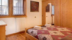 Ein Schlafzimmer mit einem hölzernen Bett, einem Heizkörper, einem Fenster mit Vorhängen und einem Spiegel.