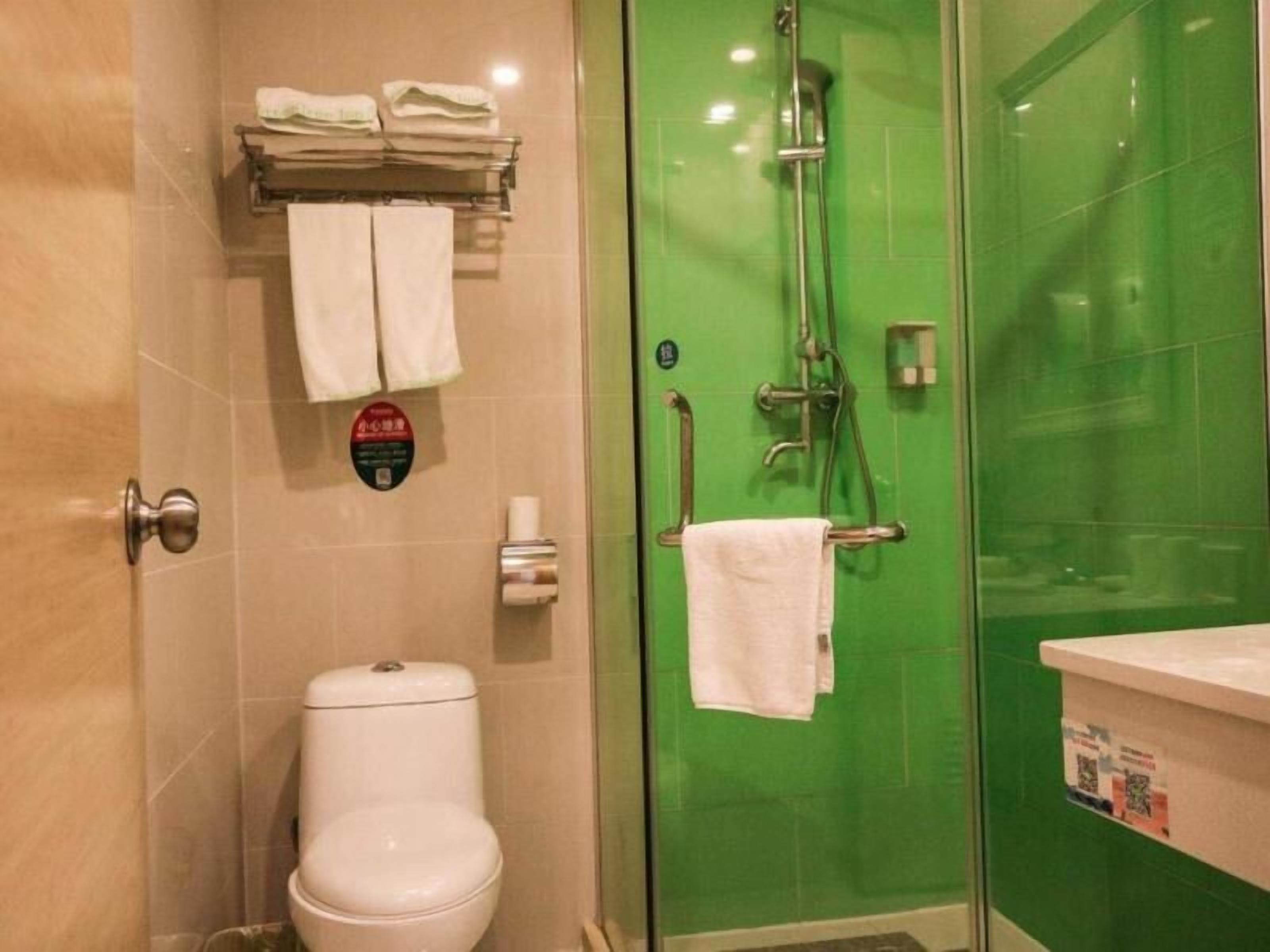 A bathroom with a toilet, a glass-enclosed shower with a green wall, and a towel rack with folded towels.