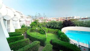 A hotel courtyard with a swimming pool, neatly trimmed hedges, and a multi-story building with a modern design. - Pretty T2 garden level at Couchant 200m from the beach in a residence with swimming pool (La Grande-Motte)