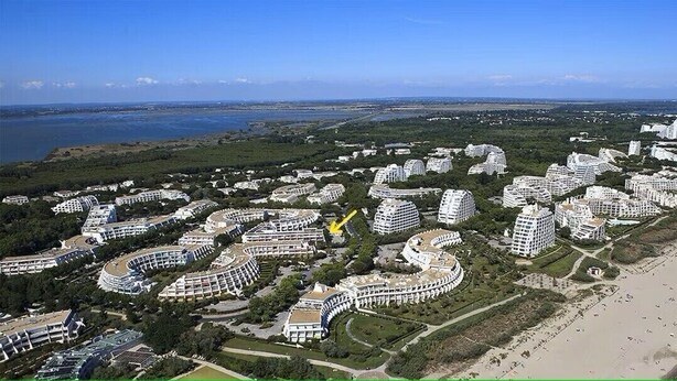 An aerial view of a coastal residential area with modern, curved buildings and a beach. - Pretty T2 garden level at Couchant 200m from the beach in a residence with swimming pool (La Grande-Motte)