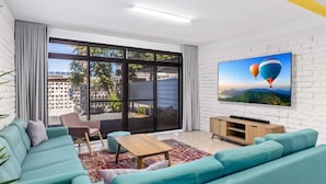 Un salon moderne avec des canapés de couleur turquoise, une table basse en bois et un téléviseur à écran plat fixé à un mur en briques blanches.
