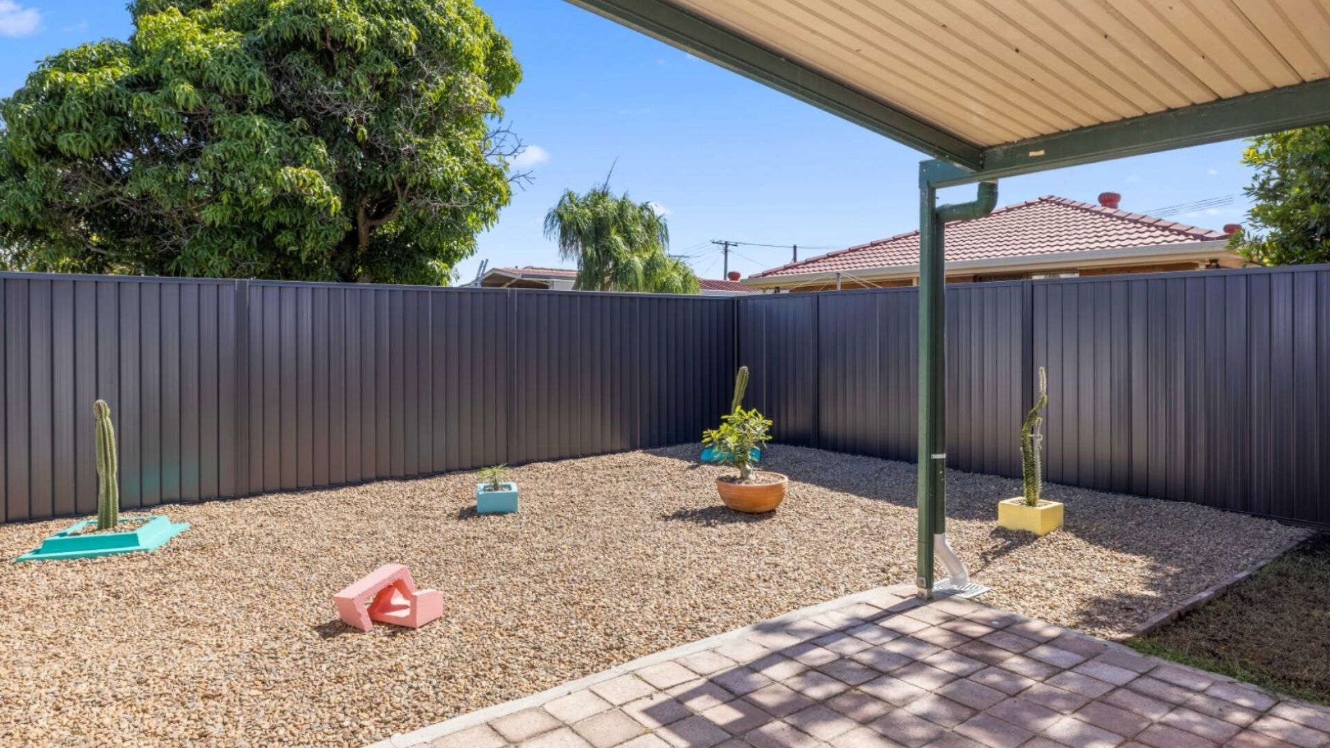A backyard with a dark fence, a small garden area with gravel, and a paved patio.