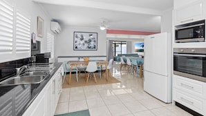 Une cuisine moderne avec des meubles blancs, un coin repas comprenant une table et des chaises, et une vue sur l’extérieur par une fenêtre.