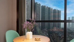 A room with a round table, two green chairs, a vase with flowers, and a plate of food. - Greentree Eastern Tongling City Beijing West Road Big Dipper City Hotel (Tongling)